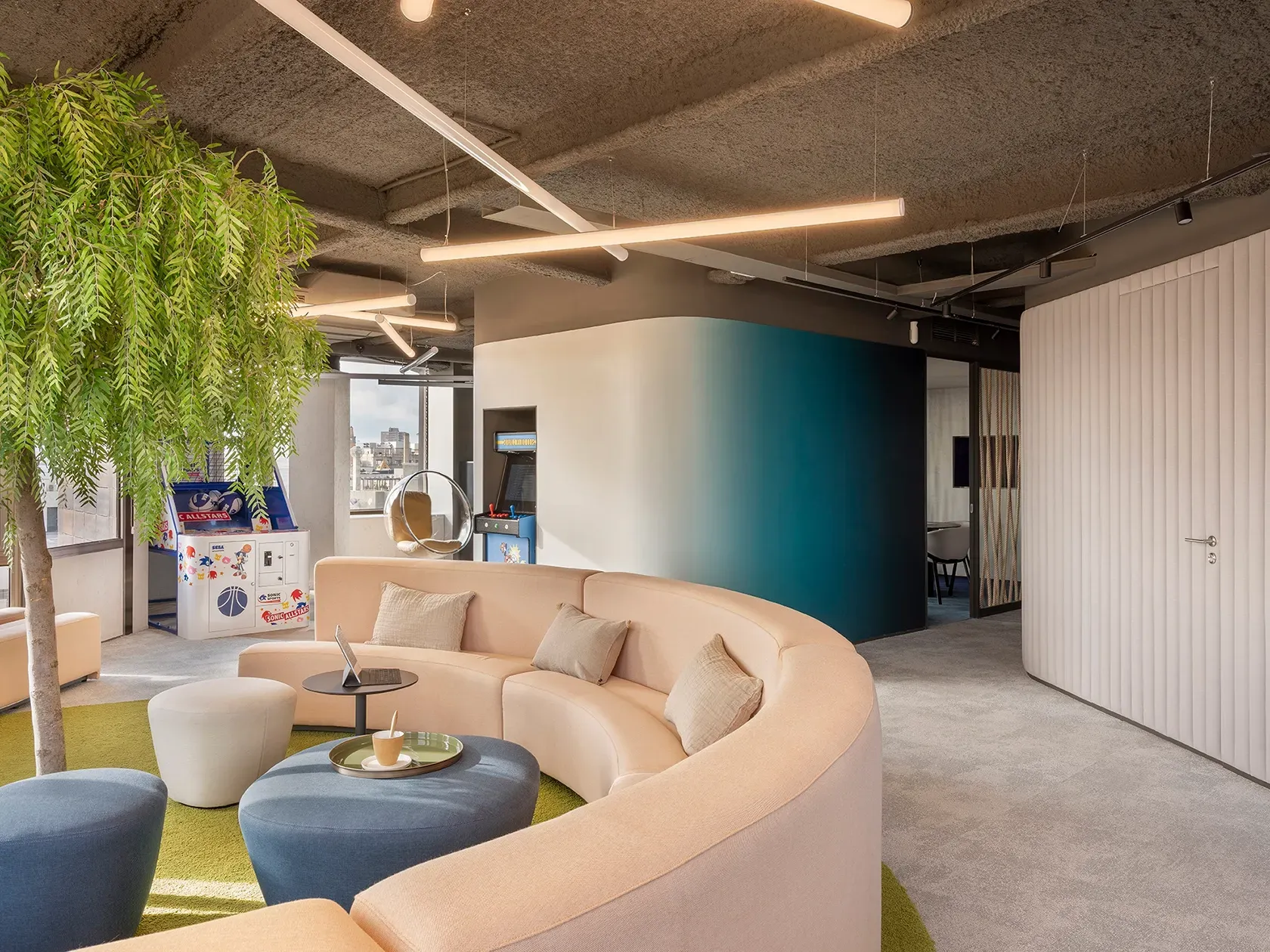 Creative lounge area with curved seating, arcade machines and natural light at LUV Studio’s Urquinaona Office