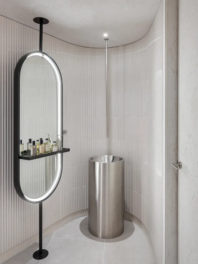 Sleek curved bathroom space with vertical tiling, designer mirror and metallic basin at LUV Studio