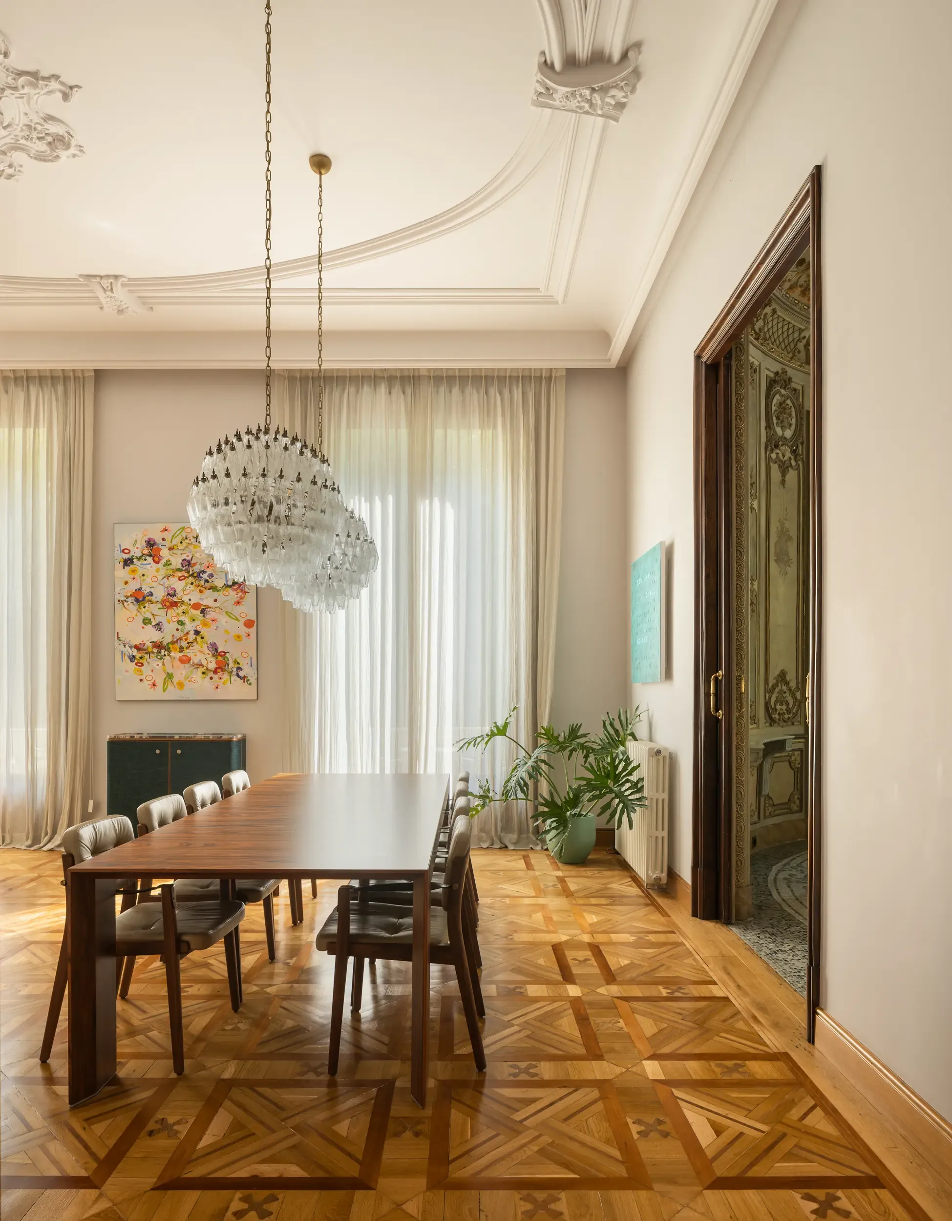 Sophisticated dining room with wooden parquet flooring, modern rectangular table, designer chairs, and crystal chandelier under decorative ceiling moldings.