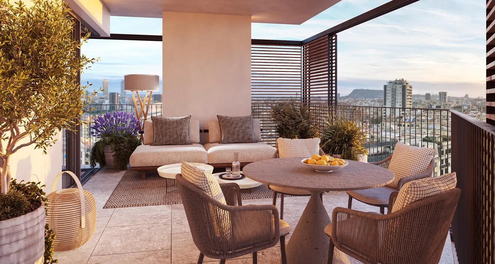 Covered rooftop terrace with cozy seating, lush potted plants and stunning sunset views over Barcelona’s skyline and Mediterranean horizon.