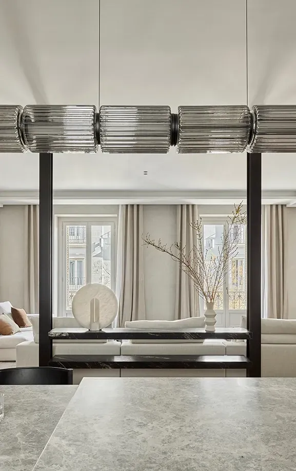 View from kitchen island towards a soft-toned living room with large windows, emphasizing the open-plan design and visual fluidity of the space.