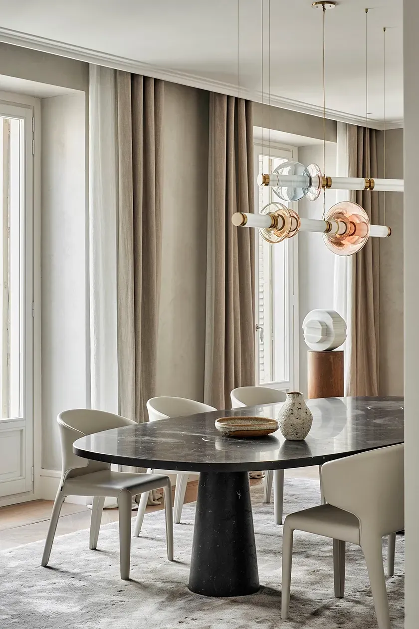 Elegant corner view of dining area with soft natural light, sculptural pendant lighting, and carefully curated ceramics on a dark stone table.