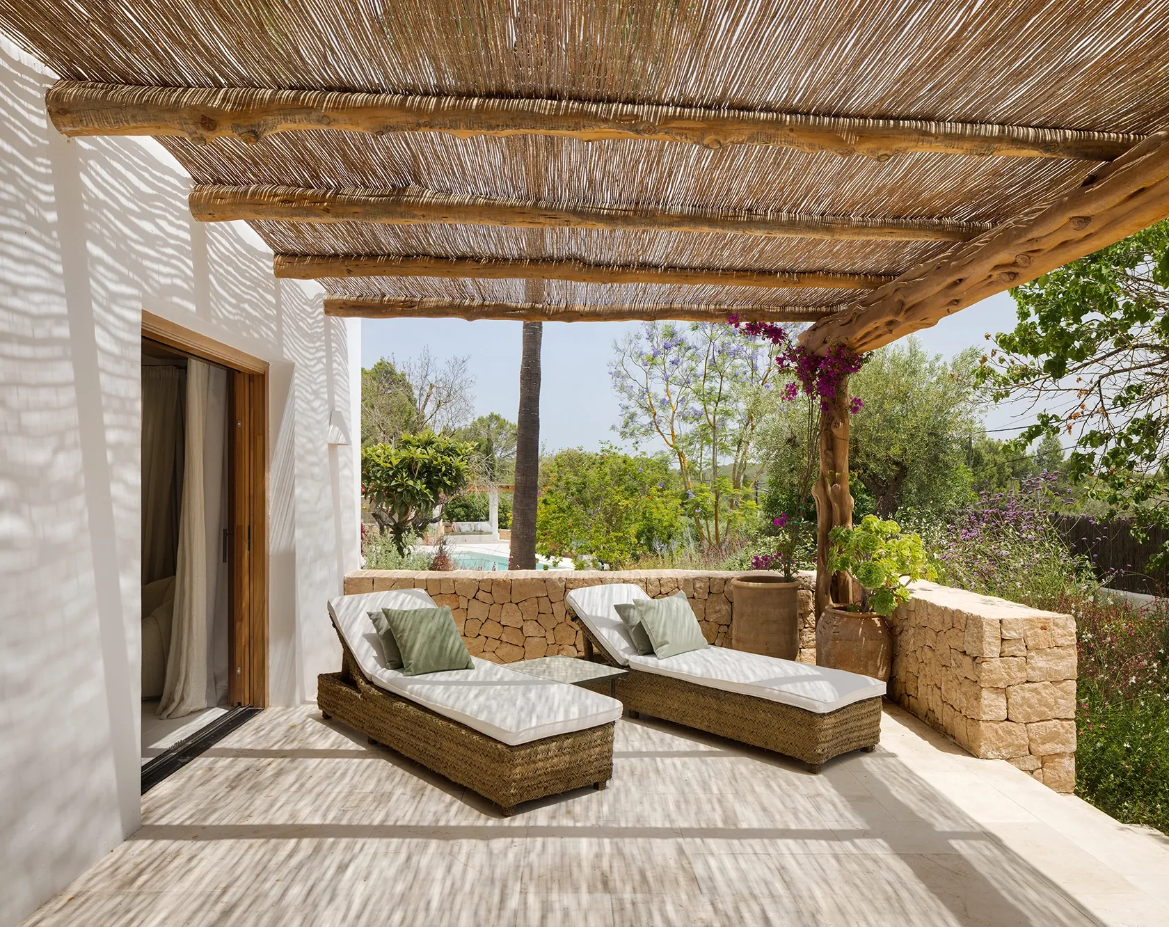 Shaded terrace with woven roof, rattan loungers, and natural stone walls offering a private retreat surrounded by Mediterranean greenery.