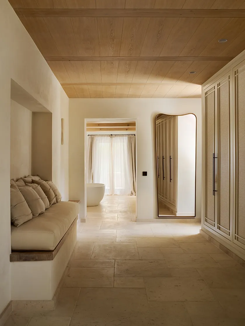 Elegant corridor with soft lighting, built-in seating, oak ceiling, and views leading to a freestanding tub in a calm spa-like bathroom.