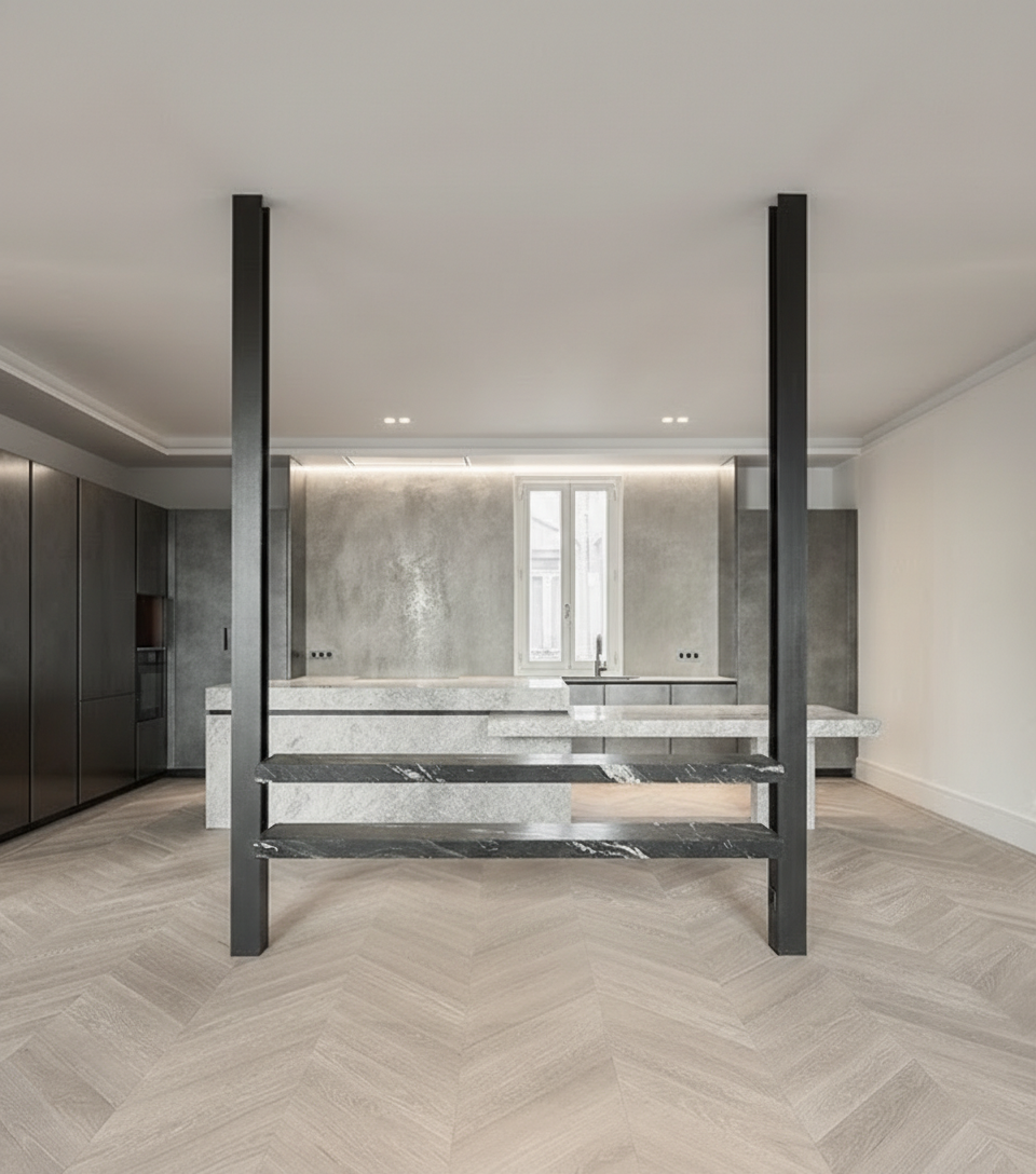 Open kitchen of the Jorge Juan Apartment featuring an integrated metal structure, a natural stone island and herringbone wooden flooring, conceived as the architectural core of the home.