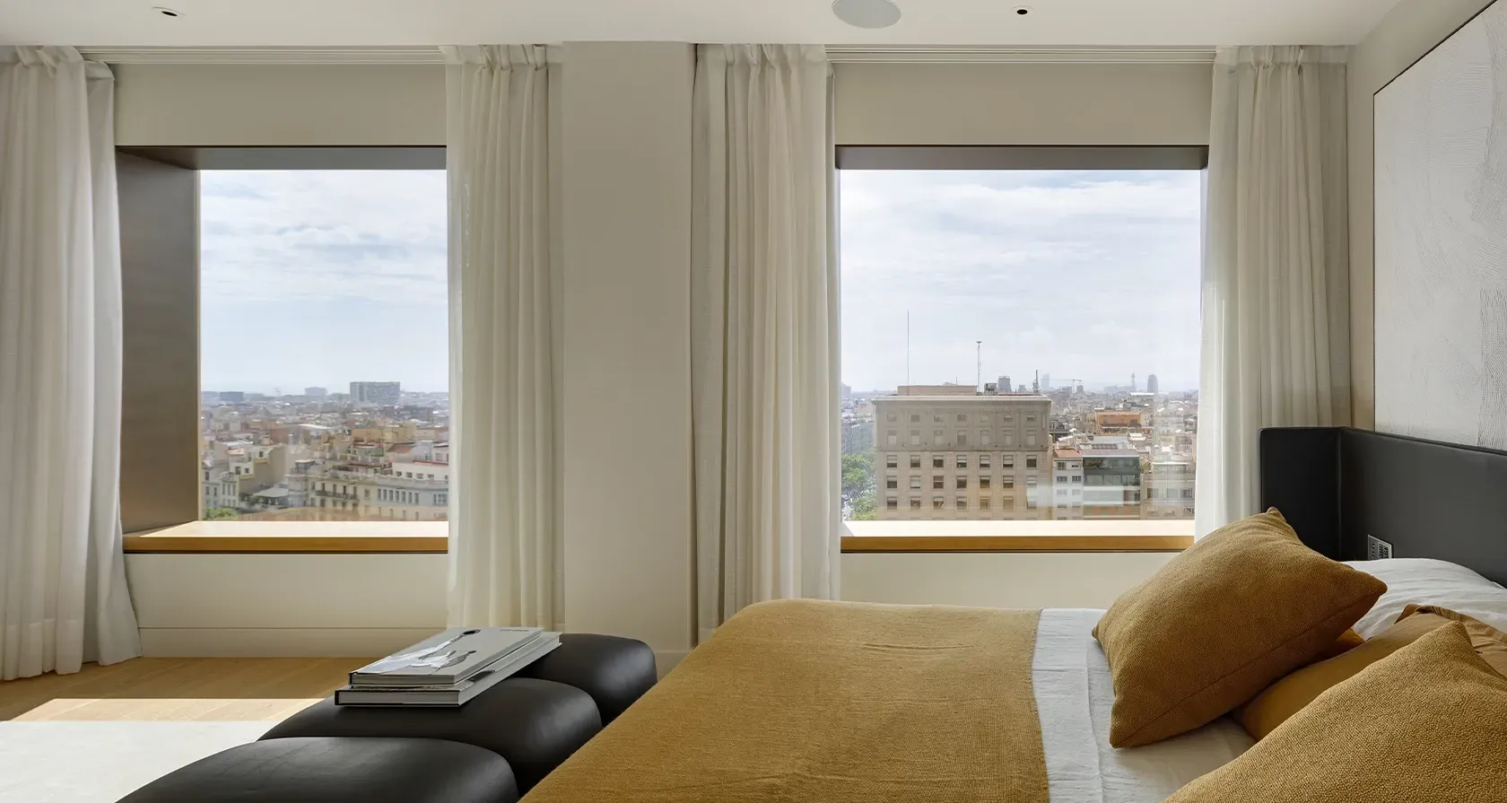 Elegant master bedroom with golden bedding and leather bench, overlooking the city from Mandarin Oriental Residences.
