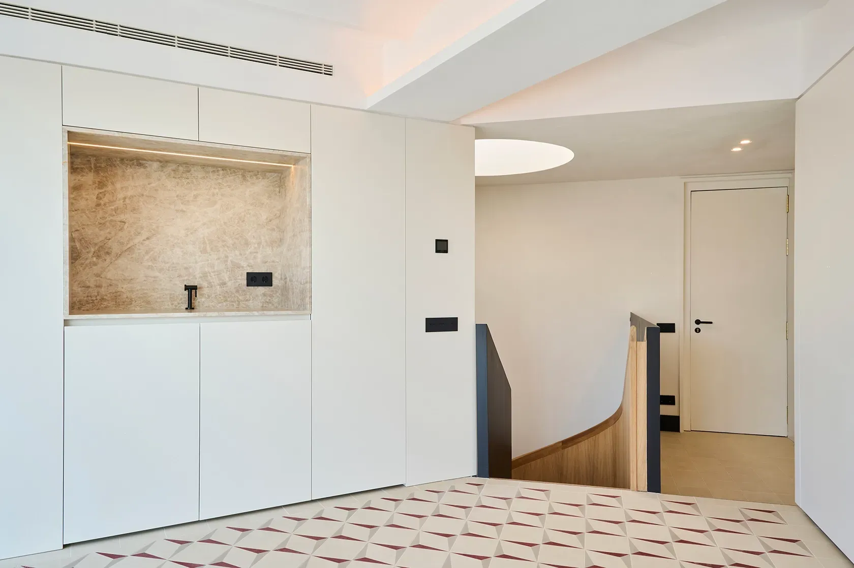 Compact kitchenette with a marble backsplash, sleek cabinetry, and black fixtures, next to a modern staircase with wood and metal details.