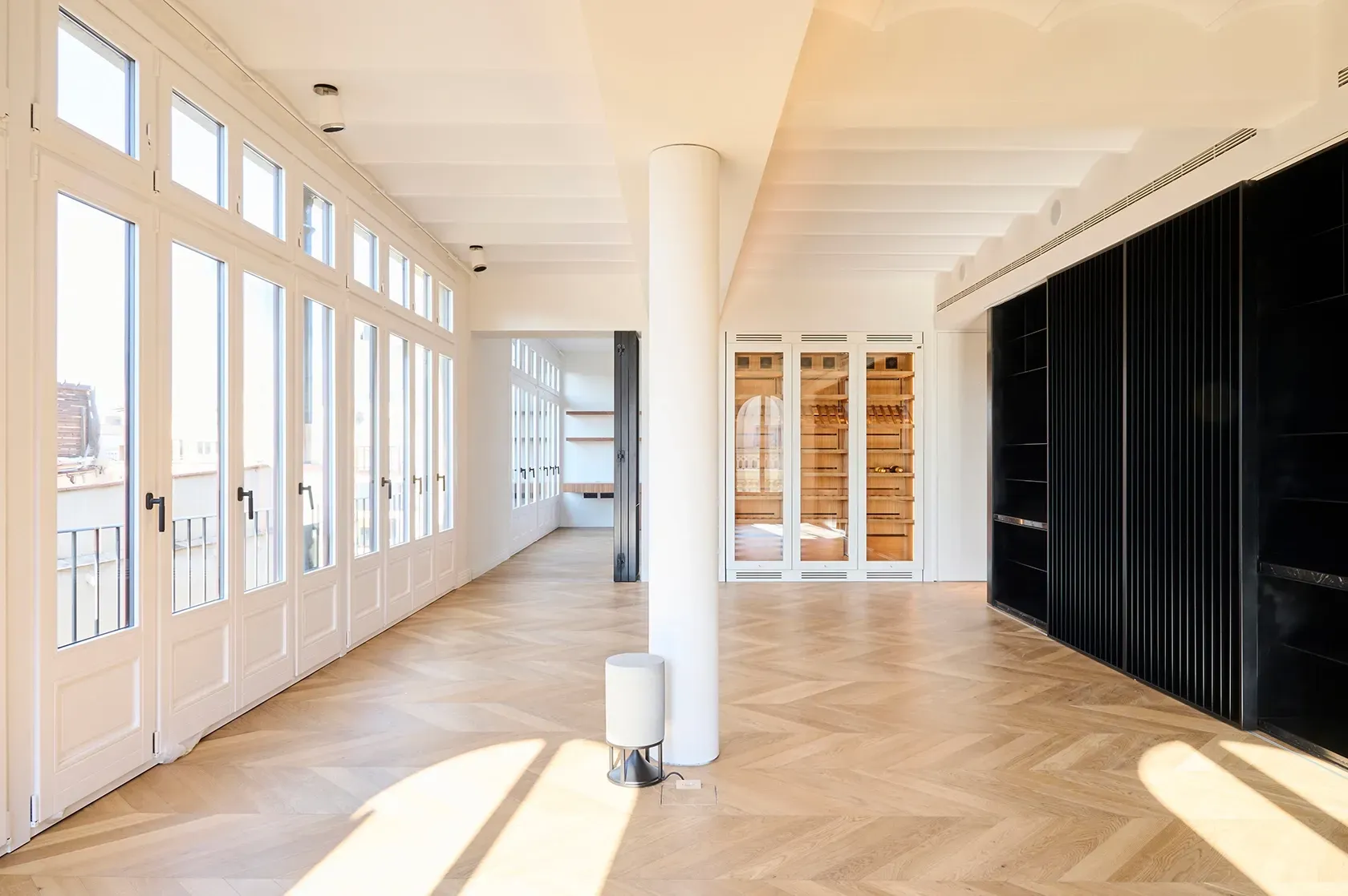 Spacious open-plan interior with large windows, natural light, chevron wood flooring, and built-in wine storage in a contemporary apartment.
