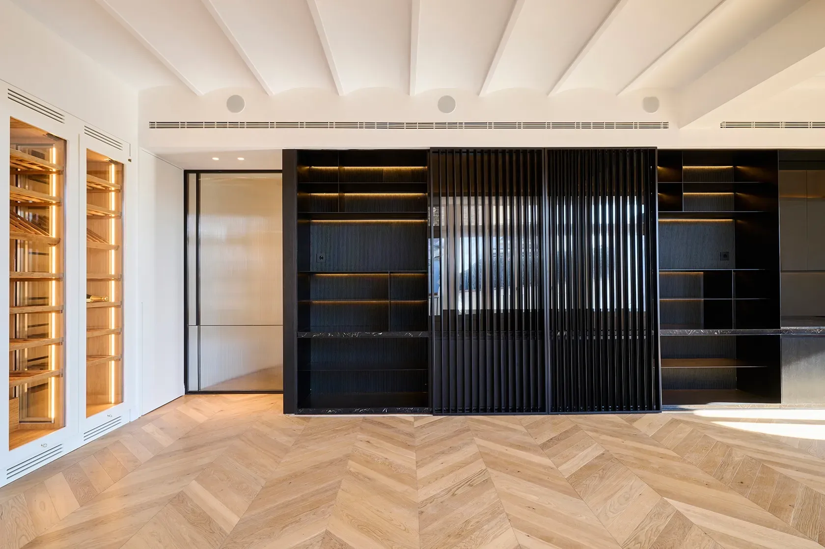 Black built-in shelving unit with integrated lighting contrasts with white walls and oak floors, highlighting the apartment’s modern elegance.