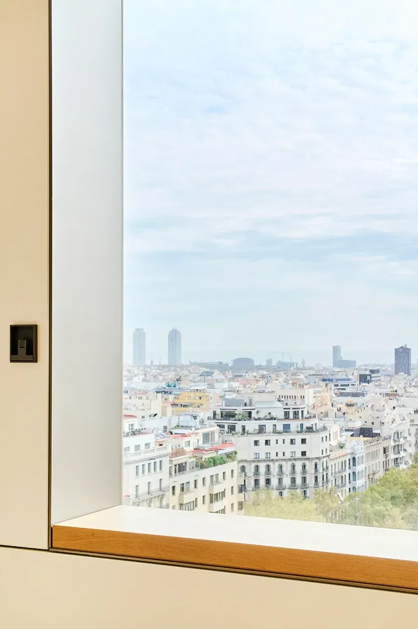 Floor-to-ceiling window framing the Barcelona skyline with views of the city and Mediterranean Sea.